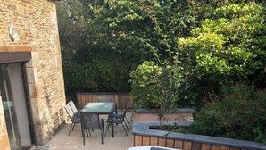 A hot tub in a backyard with a table and chairs, surrounded by greenery. - Charming gîte with Spa, on the bay of Mont Saint Michel (Sougeal)