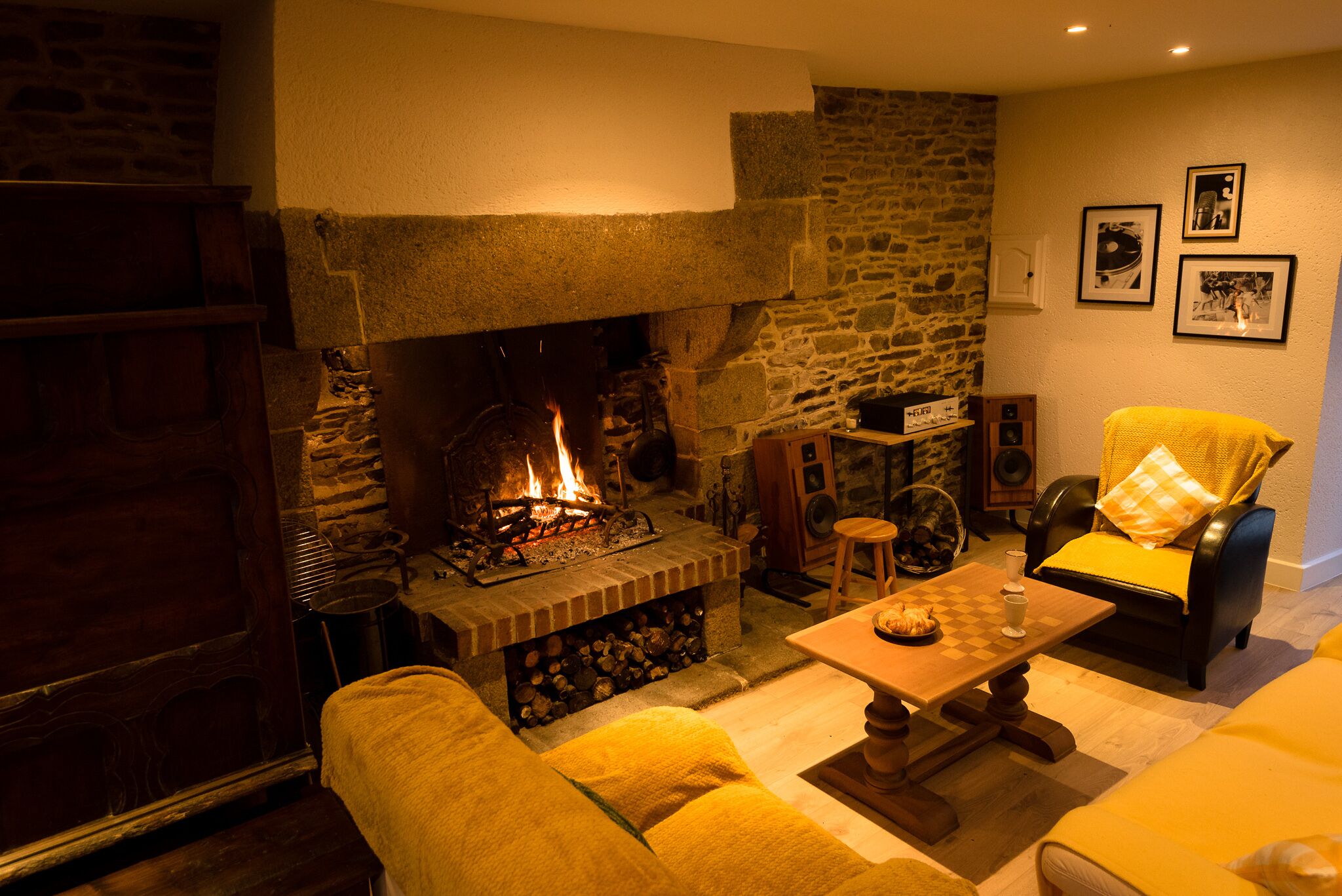 A cozy living room with a stone fireplace, a wooden table, and a yellow sofa.