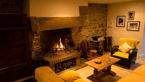 A cozy living room with a stone fireplace, a wooden table, and a yellow sofa. - Charming gîte with Spa, on the bay of Mont Saint Michel (Sougeal)