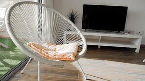 Ett modernt vardagsrum med en vit flätstol, en platt-TV och en vit TV-möbel.