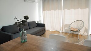 Ett modernt vardagsrum med en grå soffa, ett soffbord i trä, en glasvas med dekorativa blad och en vit stol.