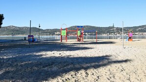 Una platja amb un parc infantil, incloent cadenes i tobogans, i una zona de sorra amb un fanal.