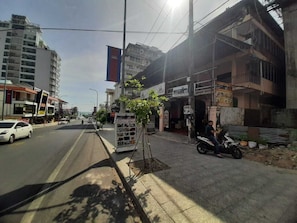 Vista de una calle con acera, un árbol, una motocicleta estacionada y edificios al fondo.