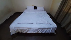 Een enkel bed met wit beddengoed, een donkere houten vloer en een effen wand met een gordijn aan de rechterkant.