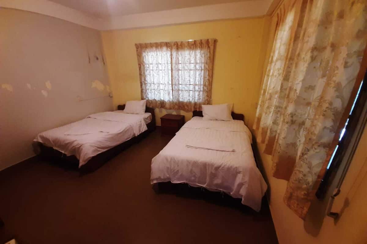 Een kamer met twee eenpersoonsbedden, een raam met gordijnen en een effen muur.