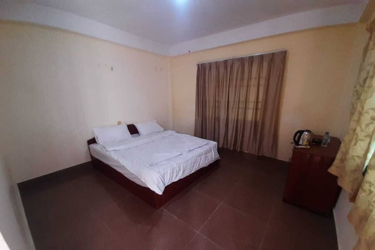 Een slaapkamer met een bed, een klein houten kastje en een gordijn.
