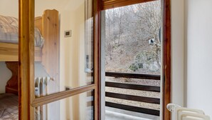 A room with a wooden bed, a window with a view of a forest, and a radiator. - Apartment 'Gianpaolo' with Mountain View, Shared Garden and Wi-Fi (Piode)