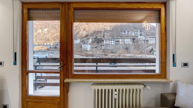 A room with a large window overlooking a village, a radiator below, and a bench outside. - Apartment 'Gianpaolo' with Mountain View, Shared Garden and Wi-Fi (Piode)