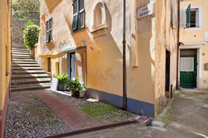 A narrow alleyway with a staircase leading to a building, a sign reading 'VIA BERONI,' and a door with a green shutter.