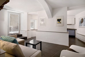 A modern living room with a sofa, a small table, and a kitchen area in the background.