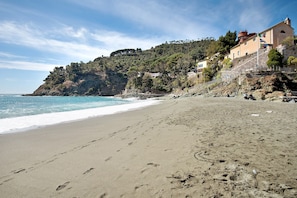 Une plage parsemée d’empreintes, un ciel dégagé et des bâtiments situés sur le flanc d’une colline.