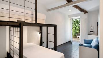 Una stanza con un letto a castello, una divano e vista su un giardino attraverso una porta aperta.