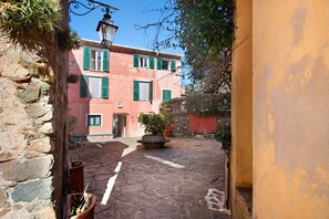 Una estrecha calle empedrada con un edificio que presenta contraventanas verdes y un muro de piedra en un lado.