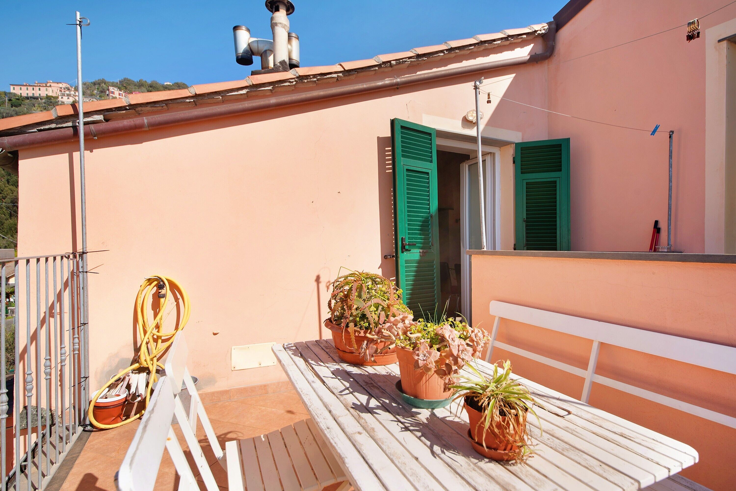 A balcony with potted plants, a hose, and a white bench.