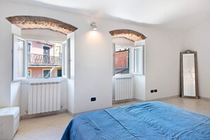 Un dormitorio con cama, ventana, radiador, espejo y balcón.
