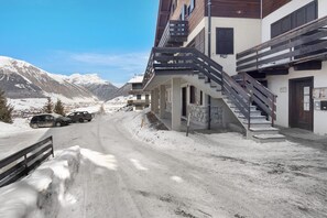 A snow-covered street with a building featuring a staircase and a balcony.