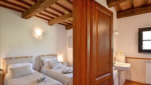 Une chambre avec deux lits, une porte en bois, un lavabo blanc et une fenêtre.