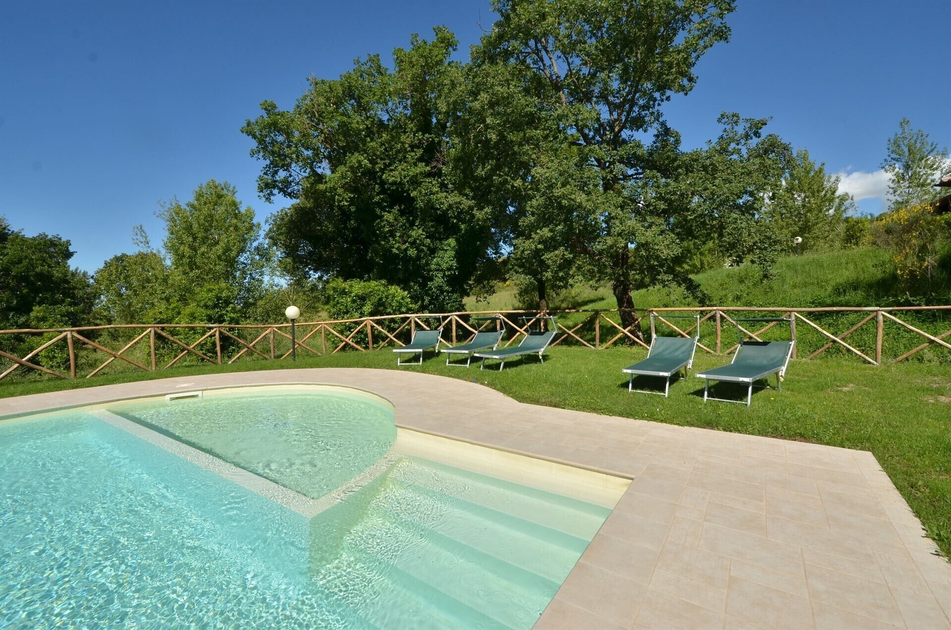 A swimming pool with clear water, surrounded by a wooden fence, and several green lounge chairs.