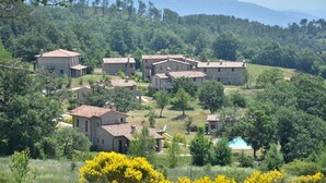 Un village rural avec des bâtiments en pierre, une piscine et un paysage montagneux en arrière-plan.