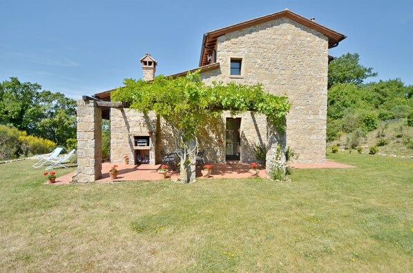 A stone house with a covered patio, a chimney, and a small window.