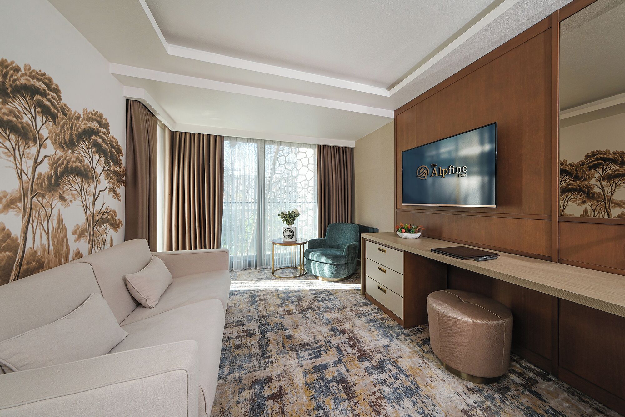 Una habitación de hotel con sofá, escritorio con televisor, silla y alfombra estampada.