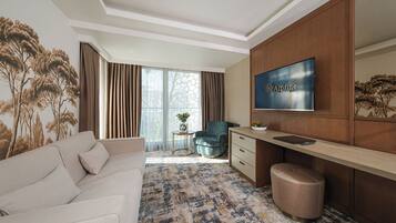 Una habitación de hotel con sofá, escritorio con televisor, silla y alfombra estampada.