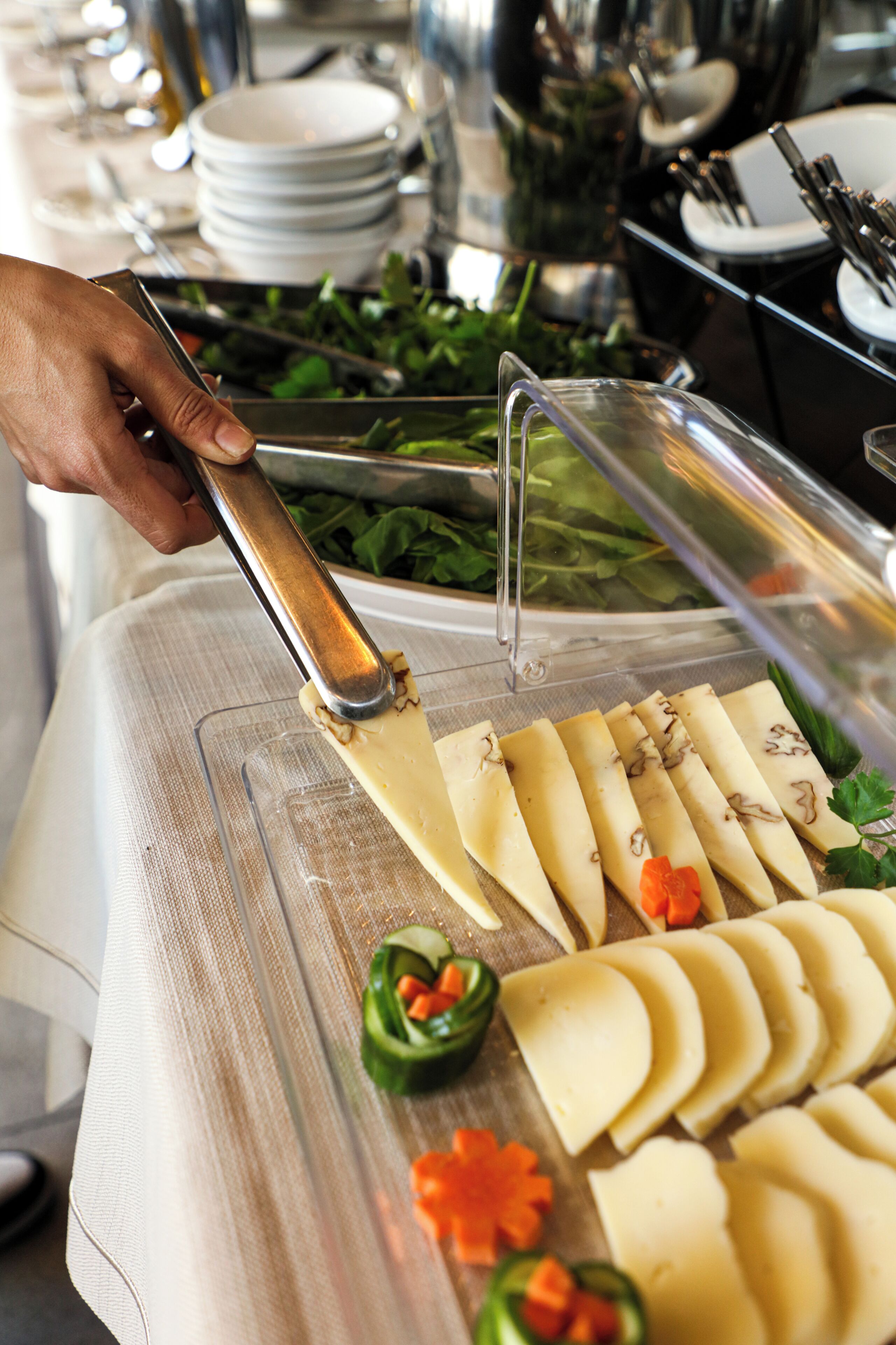 A buffet setup with a variety of food items and a hand using a knife to cut cheese.