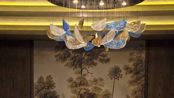 A dining area with a round table, four chairs, a chandelier, and a mural of trees on the wall.