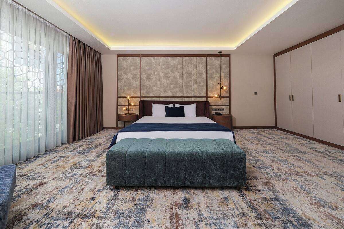 A hotel room with a large bed, a nightstand, a bedside table, a wardrobe, and a patterned carpet.