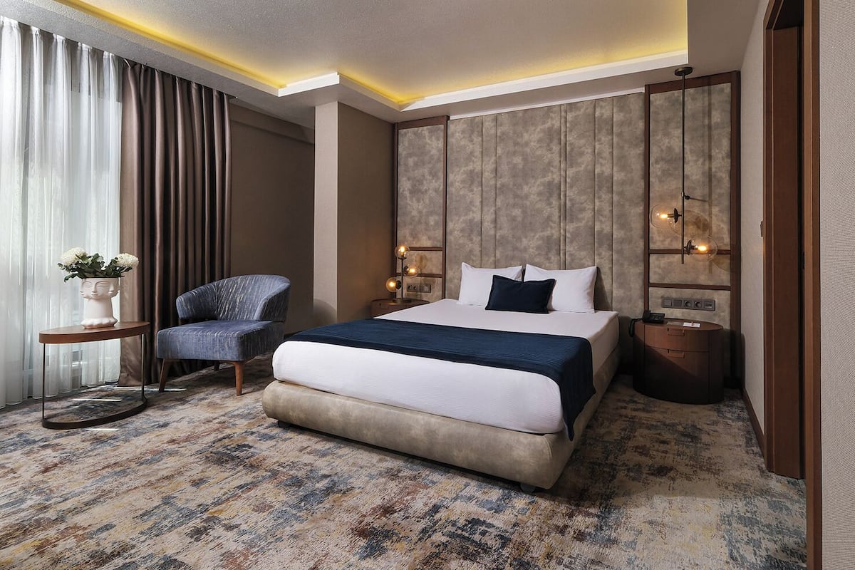 A hotel room with a bed, a chair, a bedside table, and a nightstand.