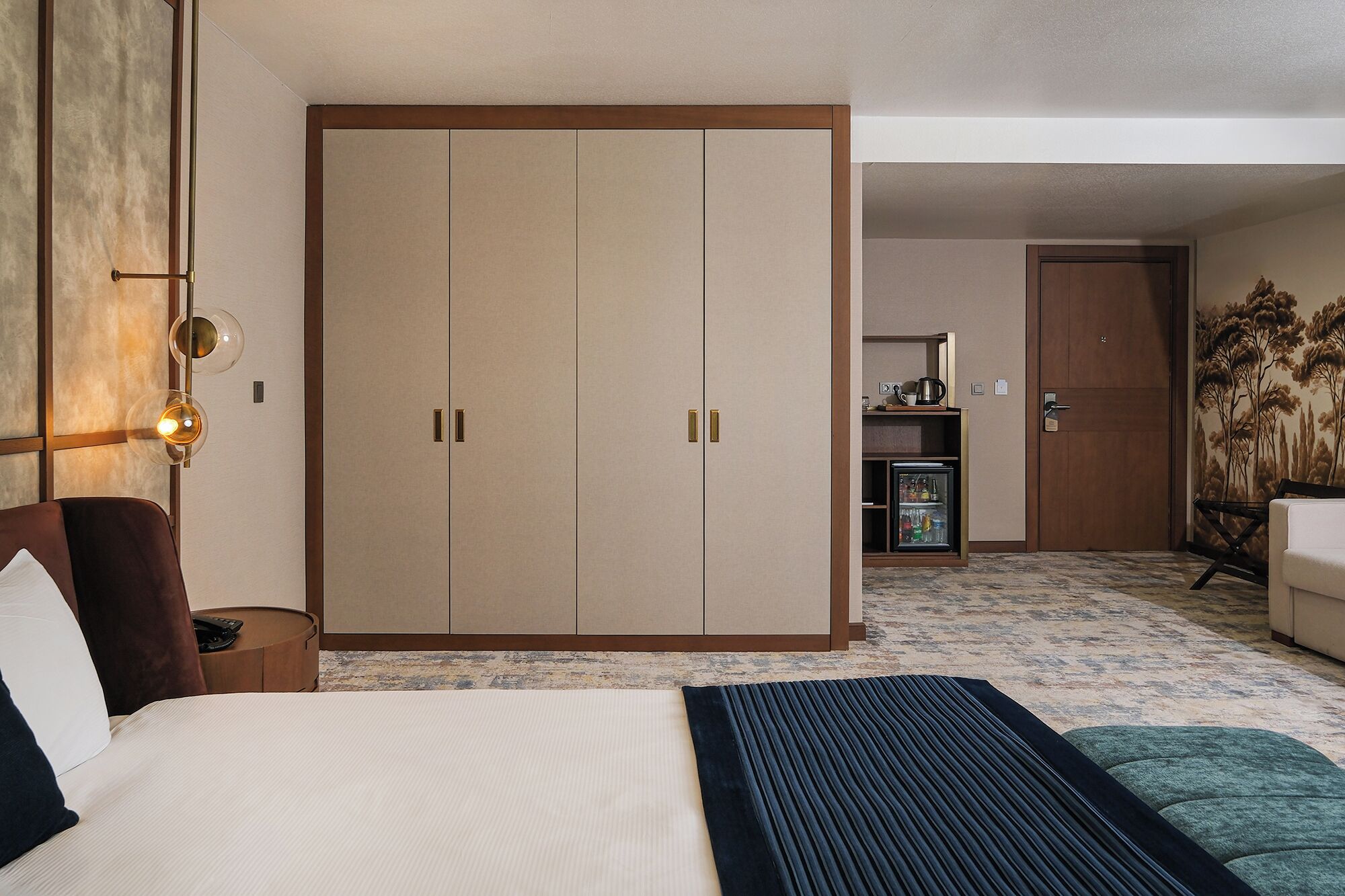 Une chambre d’hôtel comprenant un lit, une armoire, un bureau avec un réfrigérateur et un coin repas.