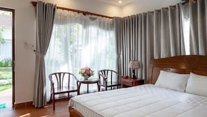 A bedroom with a large bed, two chairs, a small table with a lamp, and curtains. - LAM PHU Bungalow (Phu Quoc)