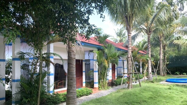 A bungalow with a red-tiled roof, surrounded by palm trees and a small garden. - LAM PHU Bungalow (Phu Quoc)