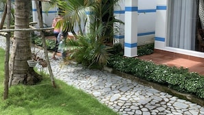 A house with a tiled roof, a stone pathway, and lush greenery including palm trees. - LAM PHU Bungalow (Phu Quoc)