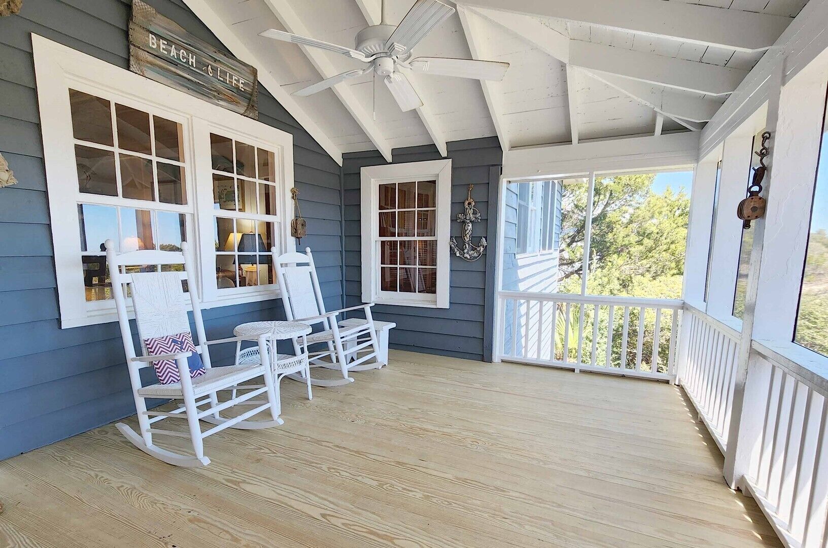A porch with white rocking chairs, a ceiling fan, and a view of the outdoors.