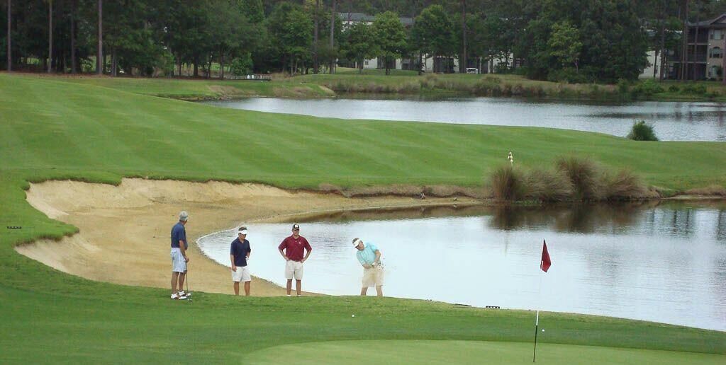 Un parcours de golf avec un obstacle d’eau et des joueurs.