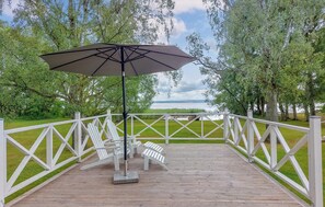 A wooden deck with white chairs and a large umbrella, overlooking a lake with a white fence and trees. - Lovely home in Höör with WiFi (Höör)
