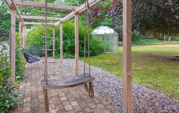 A wooden swing set with a bench, surrounded by a garden with a greenhouse and a metal chair. - Lovely home in Höör with WiFi (Höör)