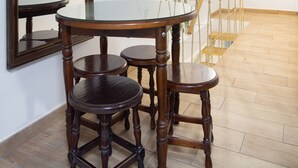 Un comedor con una mesa de vidrio y sillas de madera, un espejo grande en la pared y una lámpara con forma geométrica.