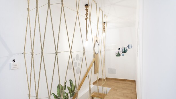 Una escalera con ceros de cuerda, escalones de madera y un espejo fijado a la pared.