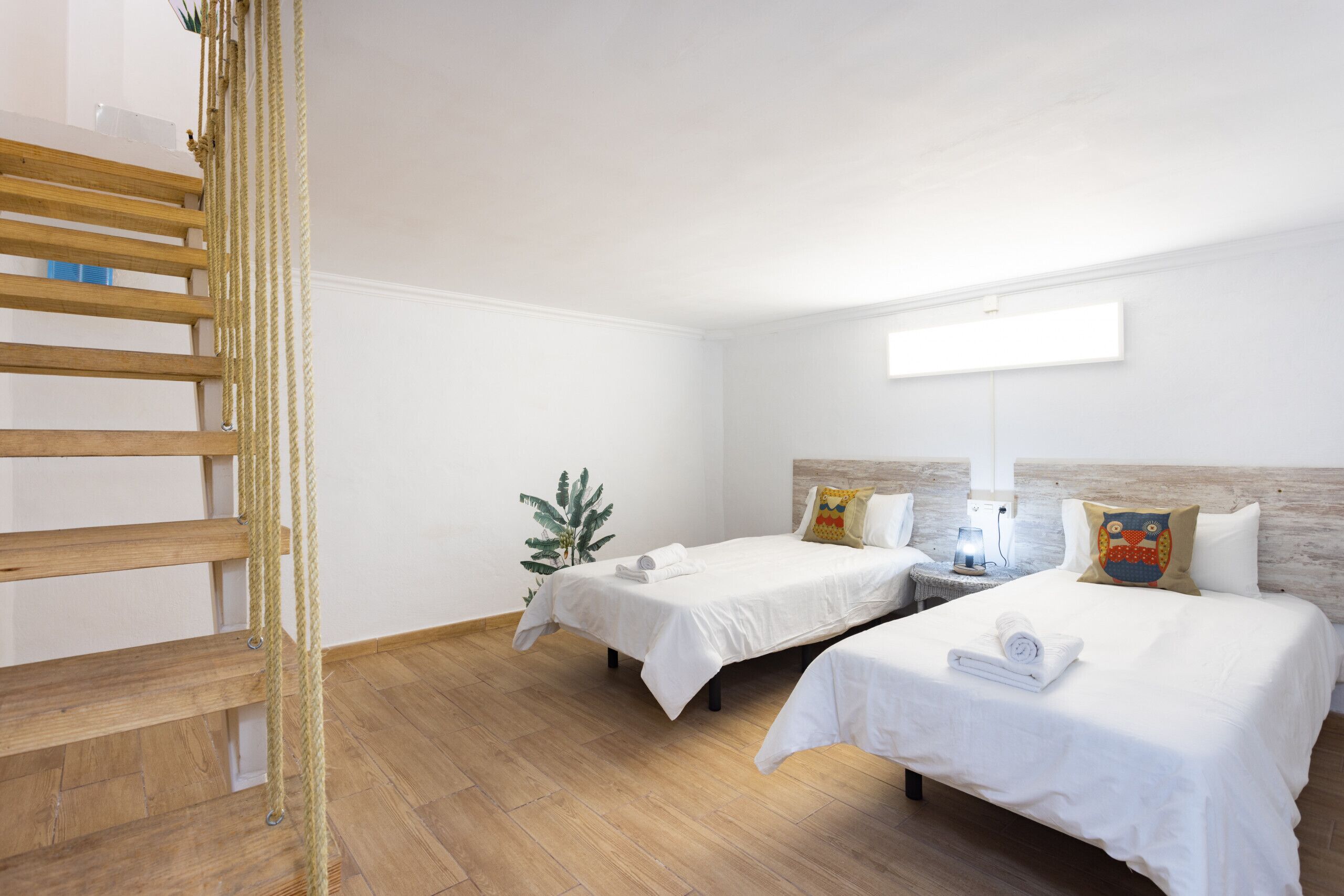 Ein Hotelzimmer mit zwei Betten, einer Holzleiter, einer Pflanze und einem Nachttisch mit Lampe.