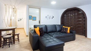 Una sala de estar moderna con un sofá de cuero negro, una mesa de comedor de madera y taburetes, y un adorno de pared.