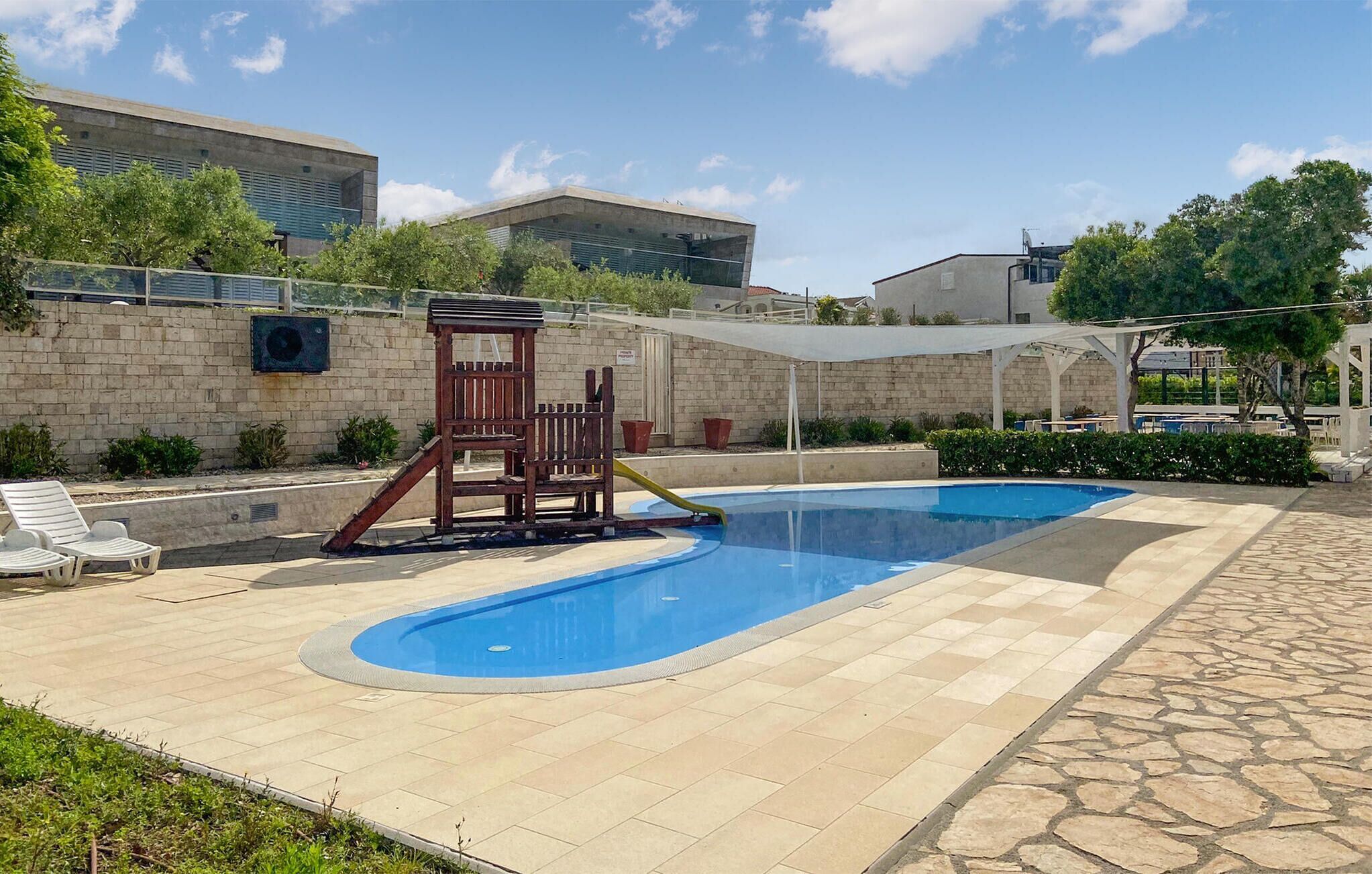A swimming pool with a slide, lounge chairs, and a play structure.