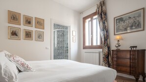 A bedroom with a bed, a dresser, a window with curtains, and six framed pictures on the wall.