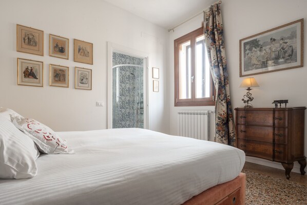 A bedroom with a bed, a dresser, a window with curtains, and six framed pictures on the wall.