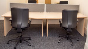 Una sala de conferencias con dos escritorios, cada uno con una silla de oficina negra. La sala tiene piso alfombrado y paredes blancas.