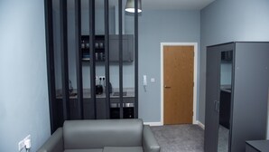 Una sala de estar moderna con un sofá gris, un armario oscuro y una cocina con armarios y encimera.