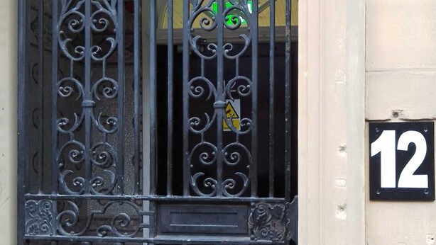 Una reja negra de hierro forjado con diseños intrincados, un cartel amarillo de advertencia y el número 12.
