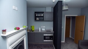 Una cocina compacta con horno empotrado, microondas y una pequeña encimera. Hay una chimenea con repisa, y una puerta que da a otra habitación.