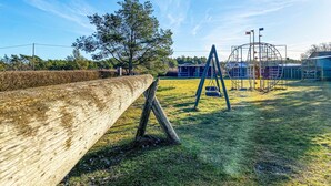 A playground with swings and a climbing structure, surrounded by a grassy field and a wooden fence. - Lovely home in Visby with WiFi (Visby)